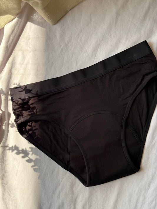 Culotte menstruelle posée sur un drap blanc, avec une lumière le long du côté gauche de l'image.