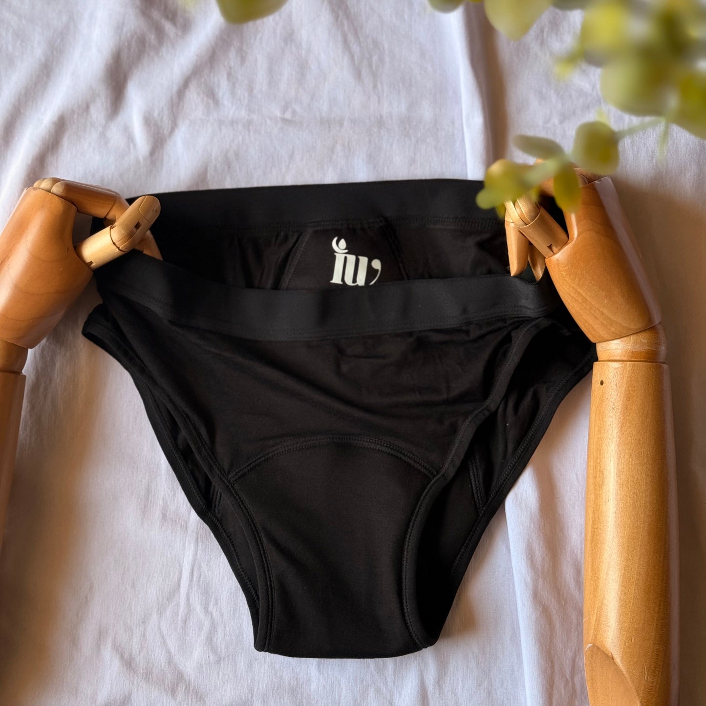 Culotte menstruelle standard présentée par un mannequin articulé en bois, avec des feuilles visibles sur le coin de l'image.