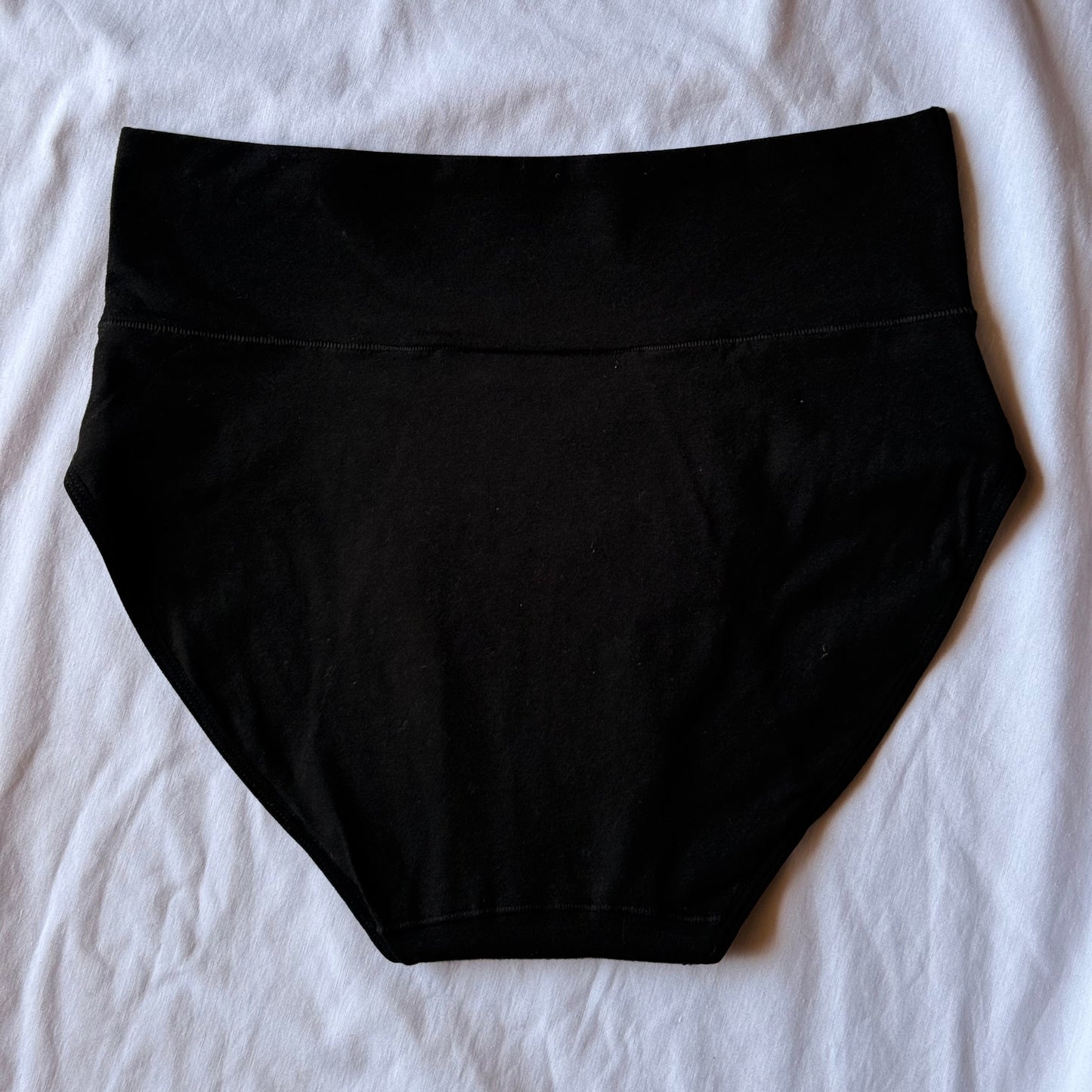Culotte menstruelle modèle taille haute vue de dos présentée sur un drap blanc.