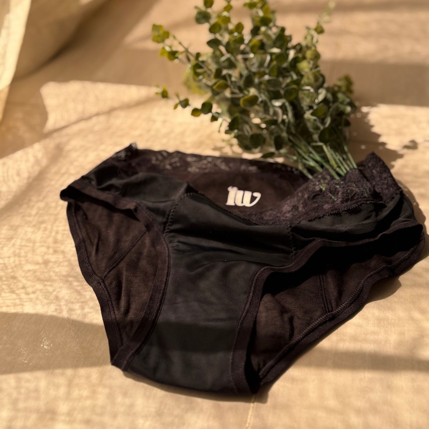 Culotte menstruelle dentelle présentée sur un fond beige, décorée d'une branche, zoomant sur le gousset, sous une lumière tamisée.