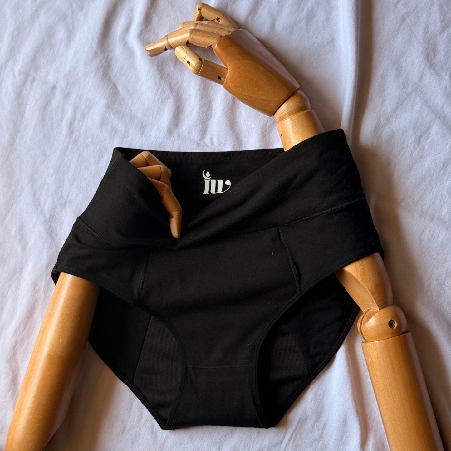 Culotte menstruelle taille haute présentée sur un mannequin en bois articulé, posé sur un drap blanc.