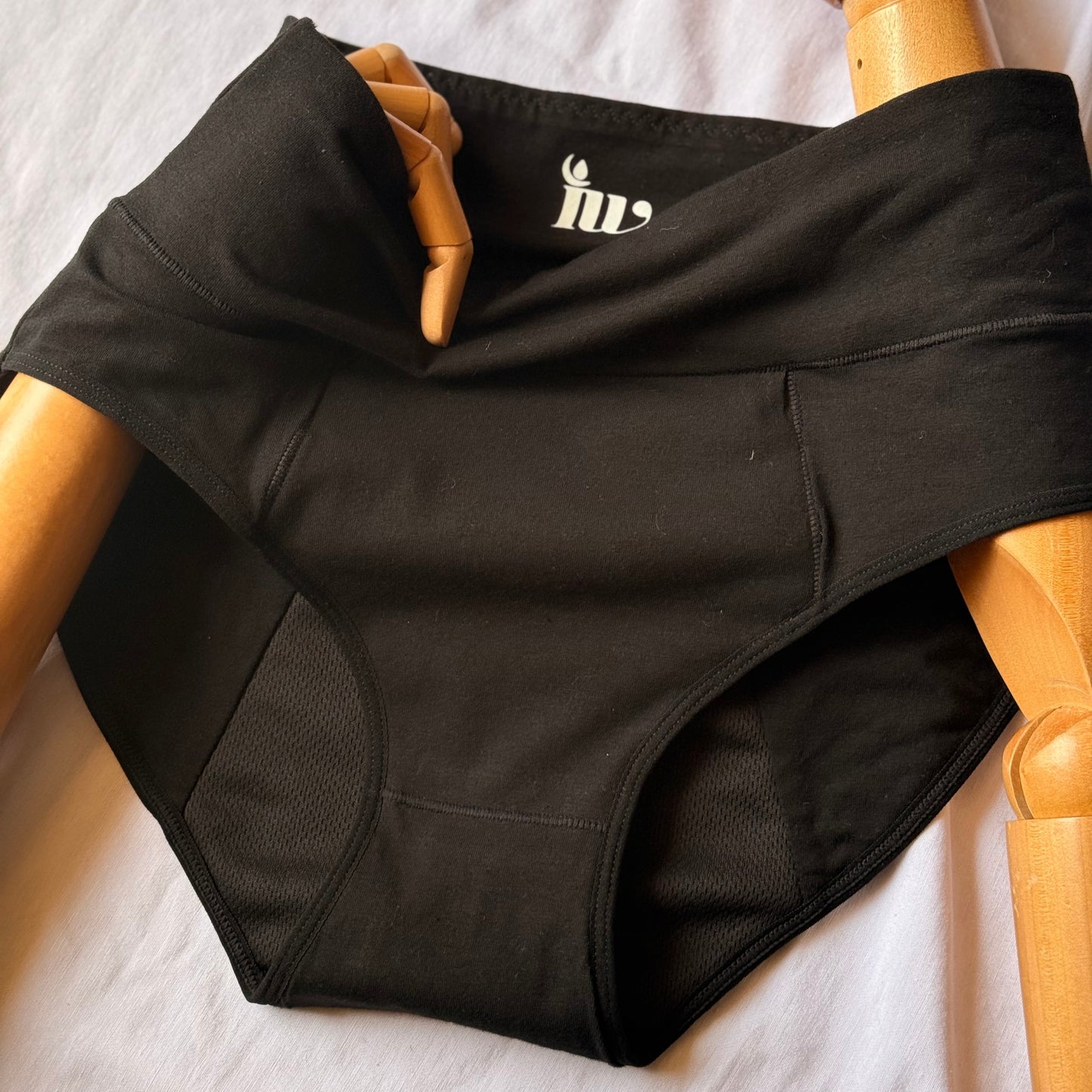Culotte menstruelle modèle taille haute en gros plan présenté sur un mannequin en bois articulé, posé sur un drap blanc.