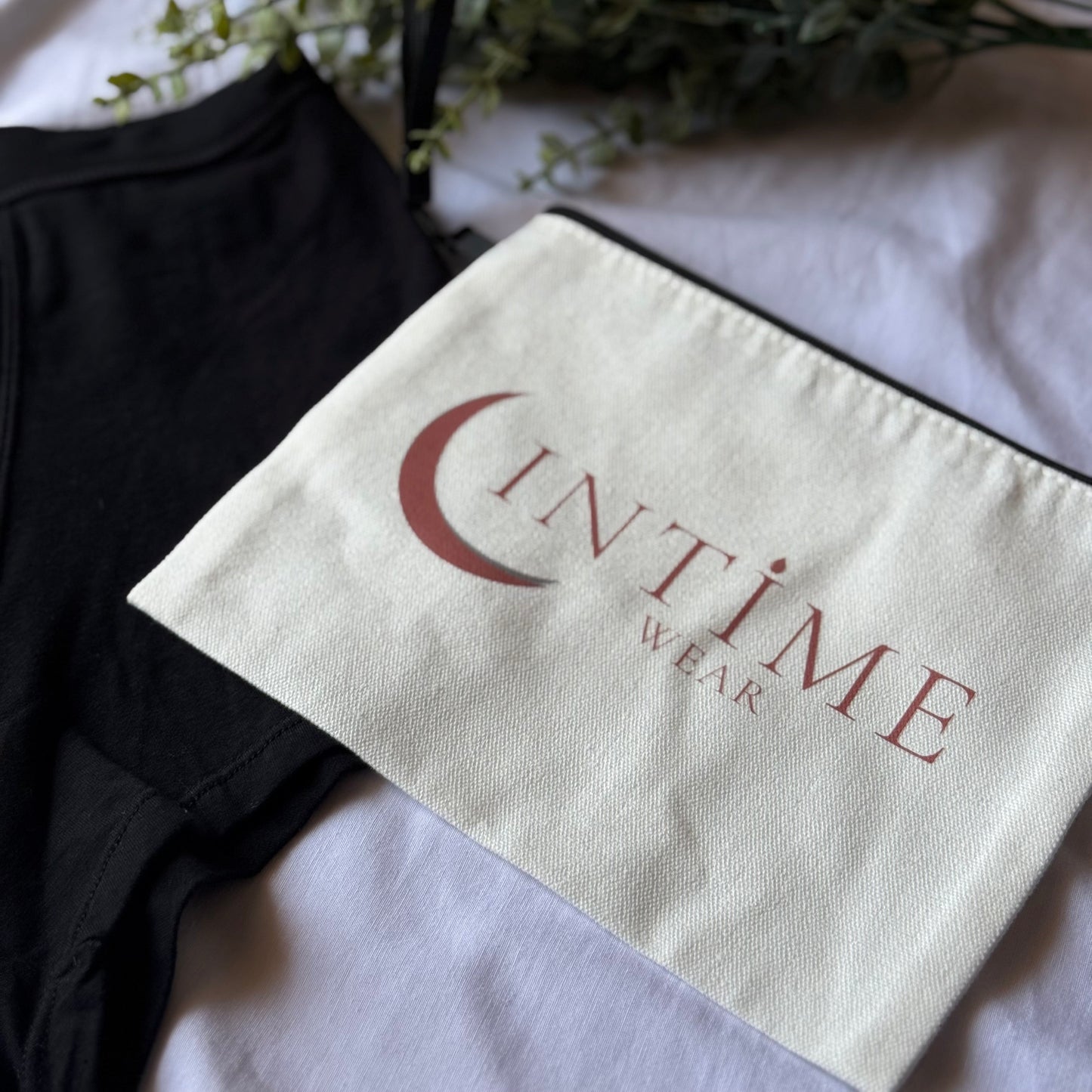 Zoom sur la pochette intime wear beige présentée sur un drap blanc, accompagnée d'une culotte nuit en coin et décorée de branches vertes.