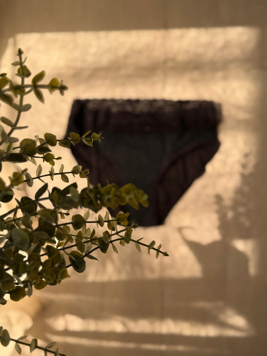 Image d'une culotte menstruelle floutée en fond avec une branche au premier plan.
