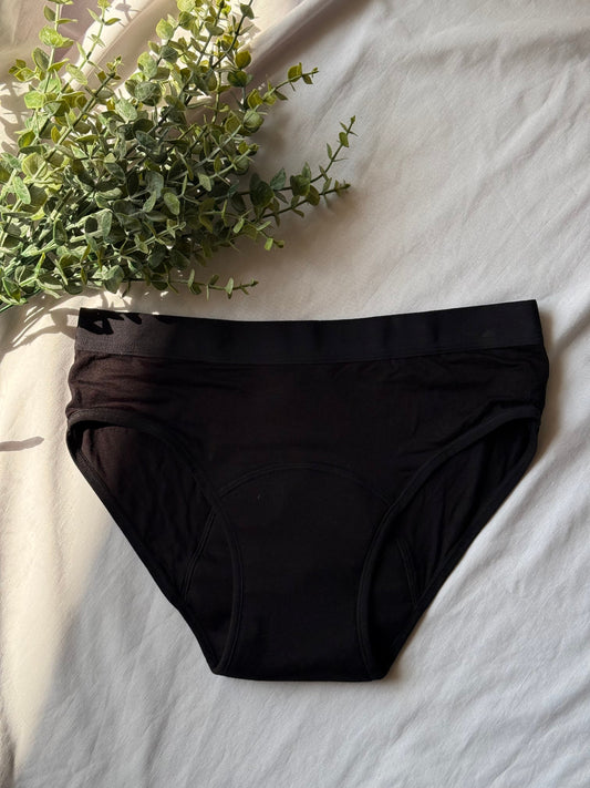 Culotte menstruelle posée sur un drap blanc, avec une branche qui décore le coin de l'image et une lumière sur le côté de l'image.