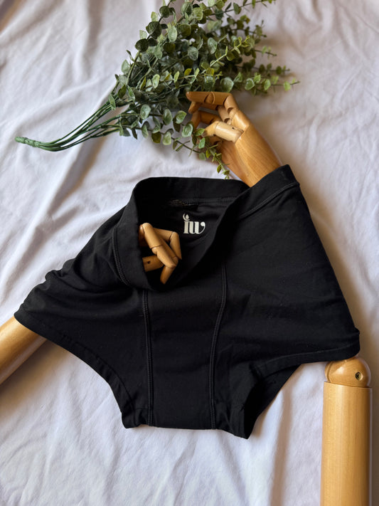 Culotte menstruelle présentée par un mannequin articulé en bois, sur une drap blanc avec une branche qui vient décorer le haut de l'image.