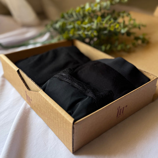 Coffret découverte féminité dans sa boite, présenté sur un drap blanc et décoré de branches vertes.
