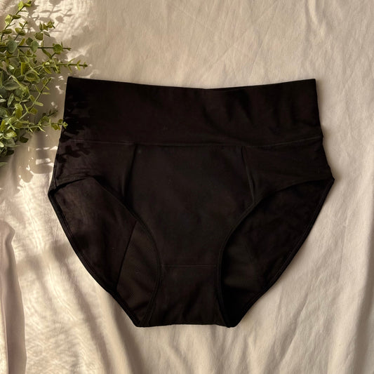 Culotte menstruelle modèle taille haute vue du dessus, présentée sur un drap blanc et décorée d'une branche.