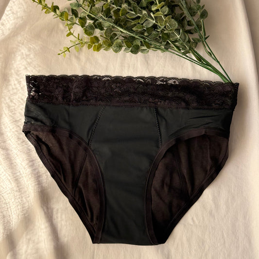 Culotte menstruelle dentelle présentée sur un drap blanc, décorée de branches, sous une lumière claire.