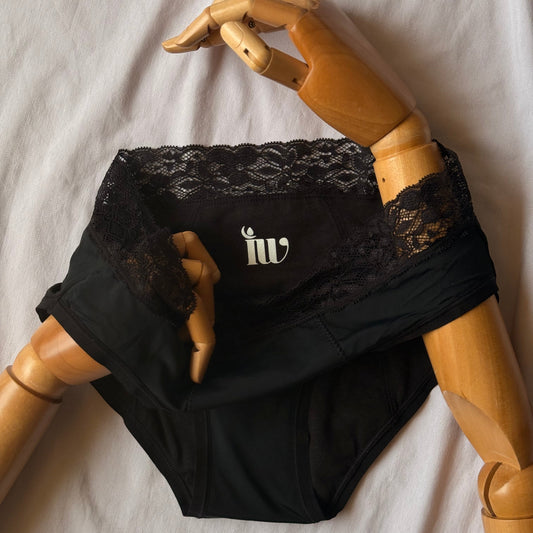 Culotte menstruelle dentelle, présentée avec un mannequin articulé en bois, sur un drap blanc et montrant le logo.