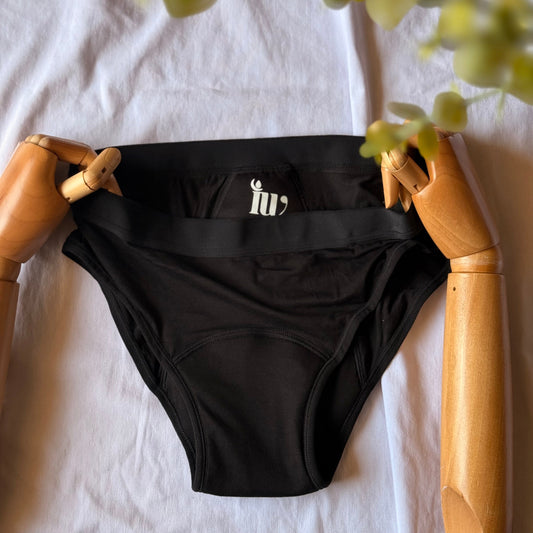 Culotte menstruelle standard présentée par un mannequin articulé en bois, avec des feuilles visibles sur le coin de l'image.
