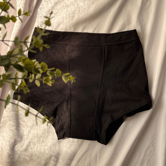 Photo de la culotte menstruelle modèle nuit, vue de haut et de face, présentée sur un drap blanc et décorée avec une branche.