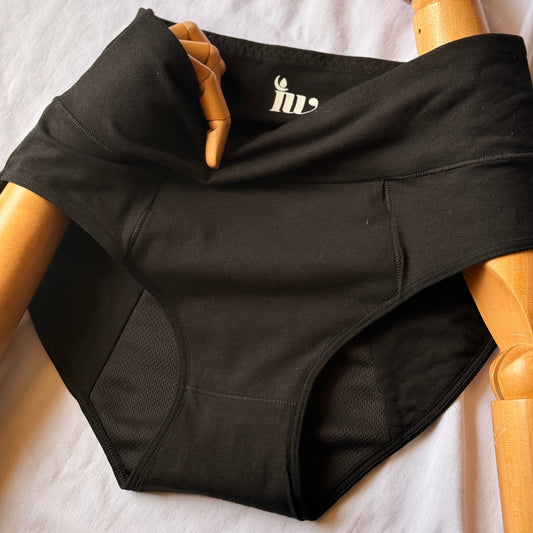 Culotte menstruelle modèle taille haute en gros plan présenté sur un mannequin en bois articulé, posé sur un drap blanc.