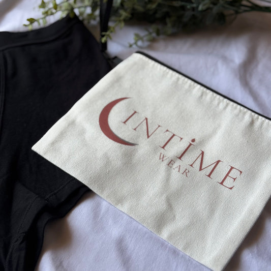 Zoom sur la pochette intime wear beige présentée sur un drap blanc, accompagnée d'une culotte nuit en coin et décorée de branches vertes.